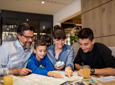 Familienurlaub im Hotel beim Kartenstudium Eine Familie sitzt an einem Tisch und betrachtet gemeinsam eine Karte oder Broschüre im Hotel.