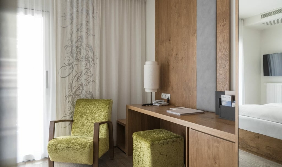 Ein heller Sitzbereich im Doppelzimmer Spatzennest mit Sessel, Hocker und Holzmöbeln.
