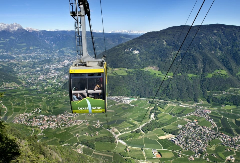 Funivia Texelbahn sulla Val Venosta in Alto Adige La funivia Texelbahn sorvola la valle con prati verdi, paesi e montagne sullo sfondo.