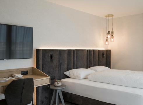 Una camera doppia arredata in stile moderno con letto, scrivania, TV e due lampade a sospensione.