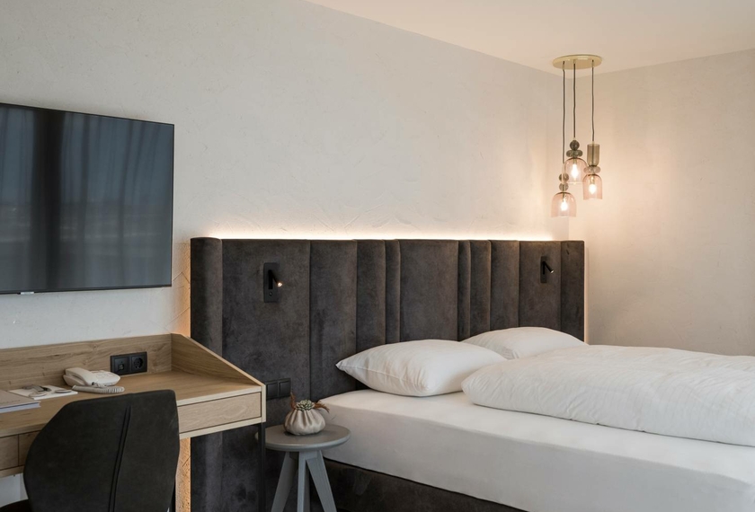 Una camera doppia arredata in stile moderno con letto, scrivania, TV e due lampade a sospensione.