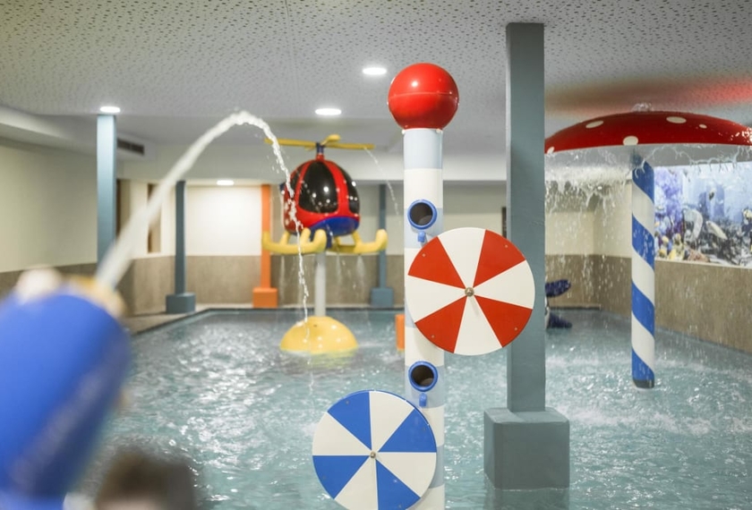Kinderpool mit Wasserspielen im Feldhof Ein Indoor-Kinderpool mit Wasserspielen und bunten Spritzelementen im Hotelbereich.