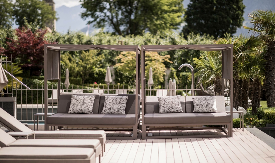 Due lettini lounge con tendine si trovano sulla terrazza in legno accanto alla piscina, nell’area giardino.