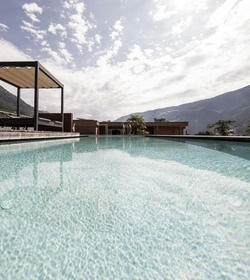 La sky infinity pool con acqua limpida si trova davanti alle montagne sotto un cielo luminoso e nuvoloso.