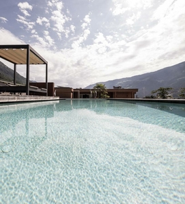 La sky infinity pool con acqua limpida si trova davanti alle montagne sotto un cielo luminoso e nuvoloso.