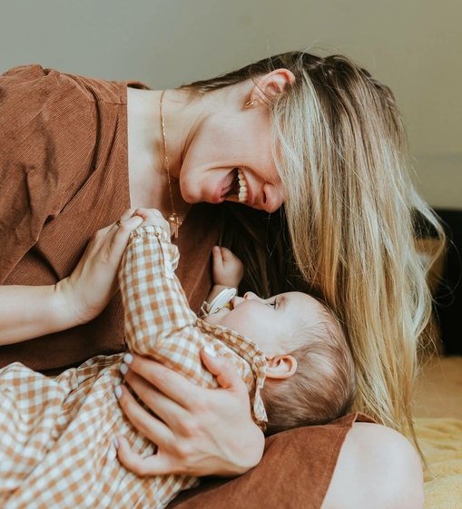 Eine Mutter lacht und hält ein Baby liebevoll im Arm.