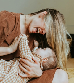 Eine Mutter lacht und hält ein Baby liebevoll im Arm.