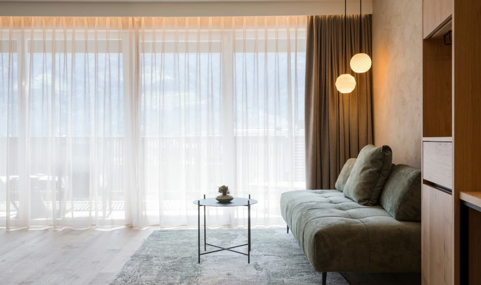 Suite Harmonie mit Sofa und Balkonfenster Ein heller Wohnbereich der Suite mit Sofa, Teppich und großem Fenster mit Vorhang.