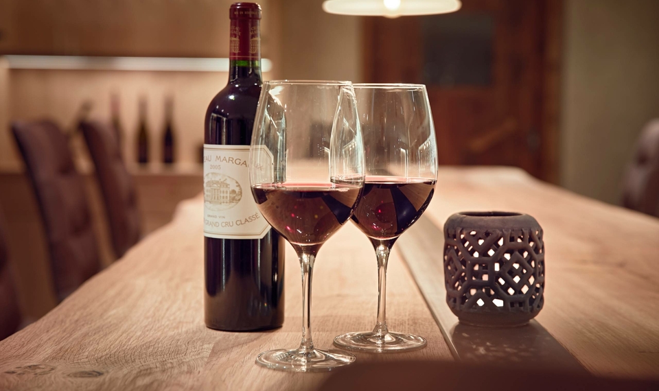 Eine Flasche Rotwein und zwei gefüllte Weingläser stehen auf einem Holztisch im Weinkeller.