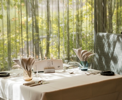 Restauranttisch im Feldhof DolceVita Resort Ein gedeckter Restauranttisch mit Menükarte, Gläsern und Besteck vor heller Fensterfront.