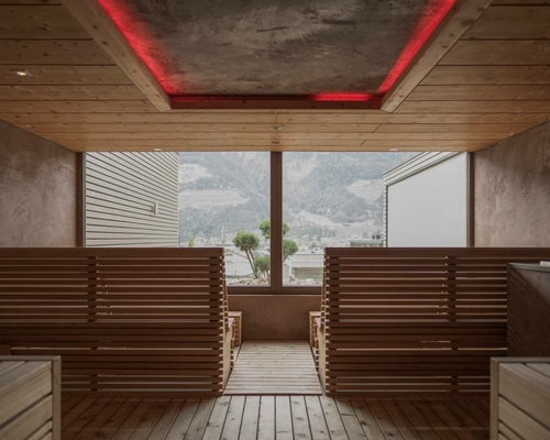 A wooden sauna with benches and a large window overlooking the mountains.