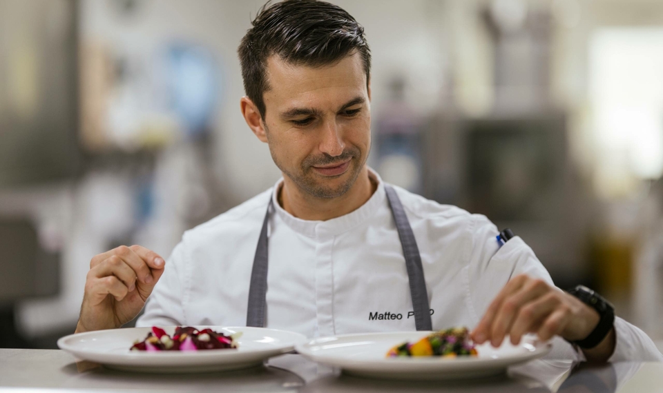 A chef plates two dishes in the hotel restaurant with careful attention to presentation.
