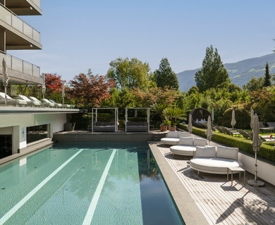 Außenpool im Feldhof DolceVita Resort Ein Außenpool mit Liegen und Sonnenschirmen neben dem Hotelgebäude und Blick auf die Berge.