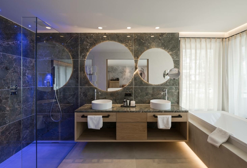 Bagno della Panorama Suite al Feldhof Resort Bagno moderno della Panorama Suite con doppio lavabo, ampia doccia e vasca accanto alla finestra.