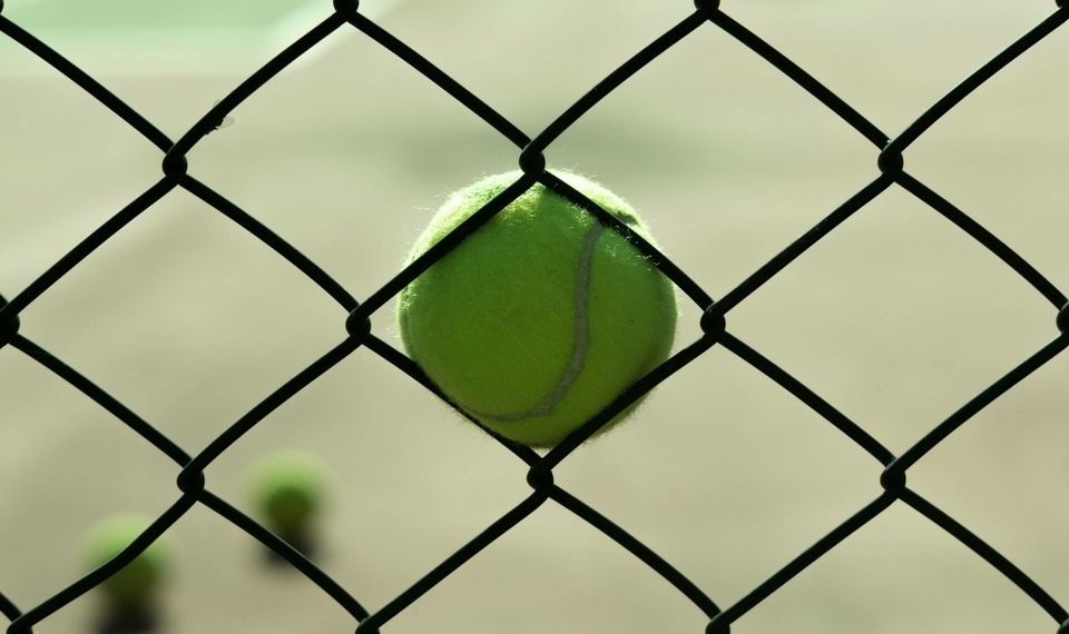 A tennis ball is caught in the chain-link fence on a tennis court.