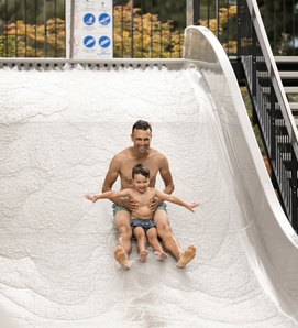 Ein Mann rutscht mit einem Kind auf einer hellen Wasserrutsche im Family Spa hinunter.