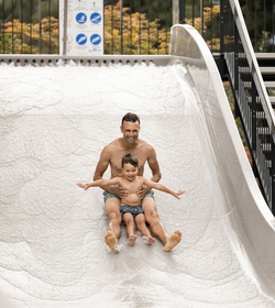 Ein Mann rutscht mit einem Kind auf einer hellen Wasserrutsche im Family Spa hinunter.