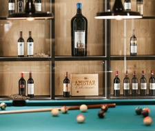 A billiard table stands in front of a shelf with wine bottles and wooden boxes.