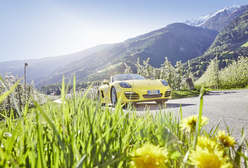 Yellow sports car on an alpine road in South Tyrol A yellow sports car is parked on a mountain road with green slopes and snow-covered peaks behind it.
