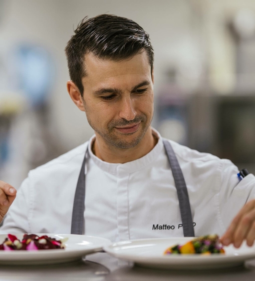 Ein Koch richtet im Hotelrestaurant mehrere Teller mit fein angerichteten Speisen an.