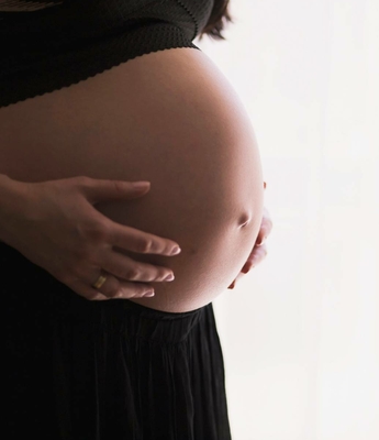 Schwangere Frau beim Wellnessbehandeln Eine schwangere Frau hält ihren Bauch mit beiden Händen vor hellem Hintergrund.