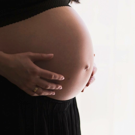 Schwangere Frau beim Wellnessbehandeln Eine schwangere Frau hält ihren Bauch mit beiden Händen vor hellem Hintergrund.