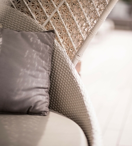 Una poltrona sospesa in rattan con cuscino grigio si trova su una terrazza in legno chiaro.