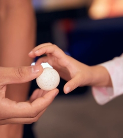Eine Kinderhand berührt einen kleinen weißen Spielball in einer erwachsenen Hand.