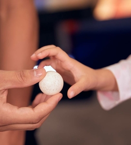 Eine Kinderhand berührt einen kleinen weißen Spielball in einer erwachsenen Hand.