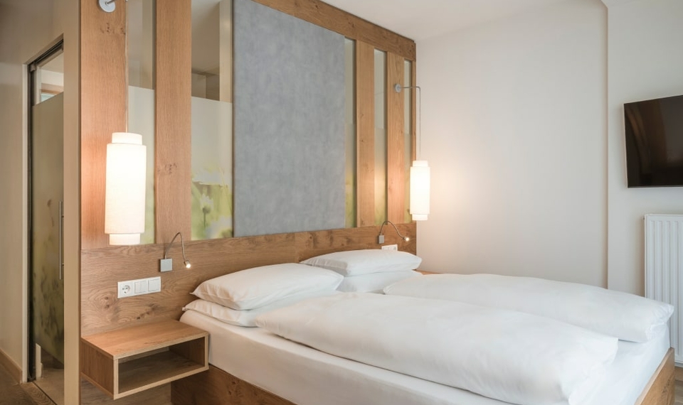 Ein Doppelbett im hellen Doppelzimmer Spatzennest mit Holzrahmen und weißen Bettwaren.