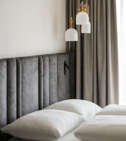 Ein Doppelbett mit gesteppten Kissen, gepolstertem Kopfteil und Vorhängen im stilvollen Hotelzimmer.