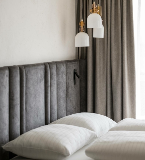Ein Doppelbett mit gesteppten Kissen, gepolstertem Kopfteil und Vorhängen im stilvollen Hotelzimmer.