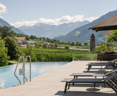 Infinity Pool im Feldhof DolceVita Resort Ein Infinity-Pool mit Liegen und Sonnenschirm mit Blick auf die Berge.