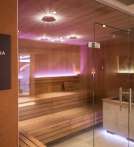 Eine verglaste Family Sauna mit warmem Licht und Holzliegen im Feldhof.