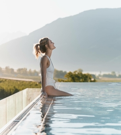 Eine Frau sitzt am Beckenrand des Infinity Pools mit Blick auf die Berge.