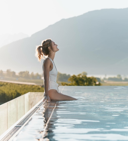 Eine Frau sitzt am Beckenrand des Infinity Pools mit Blick auf die Berge.