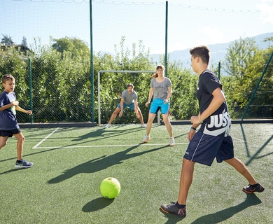 Familienurlaub in Naturns auf dem Fußballplatz Vier Kinder spielen auf einem kleinen Fußballplatz mit grünem Ball und Netzen im Hintergrund.