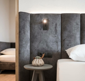 A hotel room with a dark grey upholstered headboard, bedside table and bed in a calm interior.