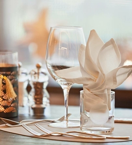 Ein elegant gedeckter Tisch mit Weinglas, Besteck und gefalteter Serviette in einem Hotelrestaurant.
