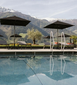 Una piscina a sfioro con lettini e ombrelloni davanti a un panorama montano e cime innevate.