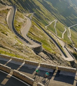 Two cyclists ride along the winding pass road through the mountain landscape in South Tyrol.