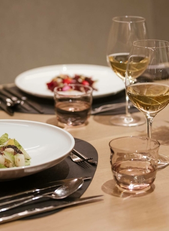 A set dining table shows plated dishes, wine glasses and water glasses in a warm restaurant setting.