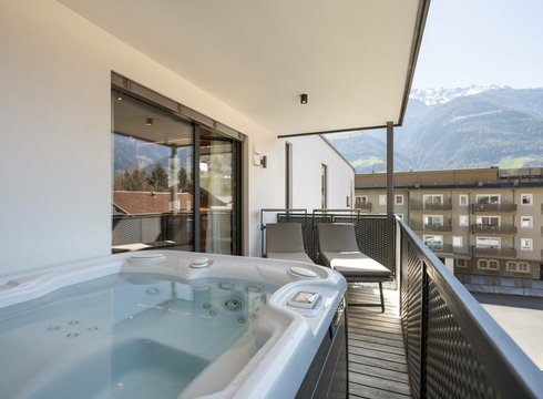 Il balcone del chalet mostra una whirlpool privata, due lettini e la vista sulle montagne e sugli edifici vicini.