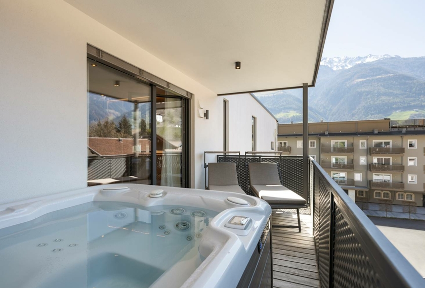 Il balcone del chalet mostra una whirlpool privata, due lettini e la vista sulle montagne e sugli edifici vicini.