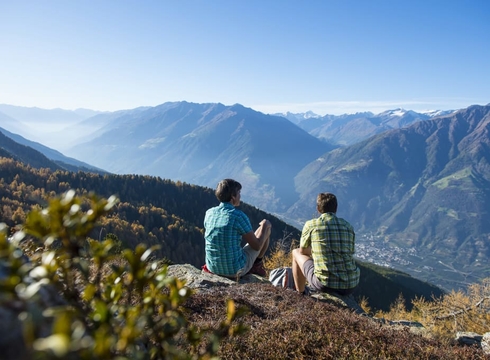 Escursioni a Naturno con panorama alpino Due escursionisti siedono su uno sperone roccioso e guardano il vasto paesaggio montano.