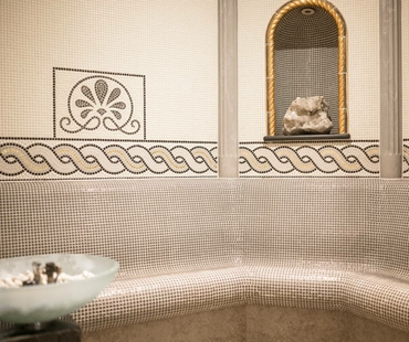 Eine Mosaiksauna mit gebogener Sitzbank, Wandornamenten und einer Nische mit Dekosteinen.