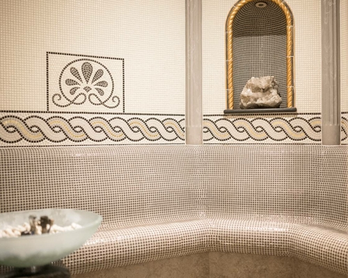 Eine Mosaiksauna mit gebogener Sitzbank, Wandornamenten und einer Nische mit Dekosteinen.