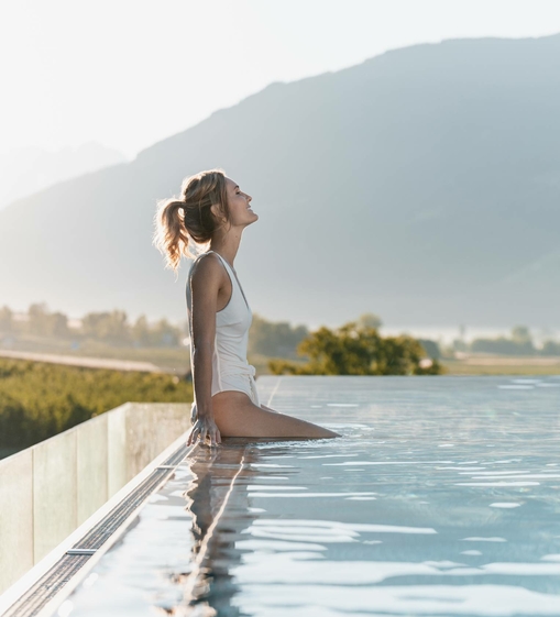 Eine Frau sitzt am Rand des Sky Infinity Pools und blickt in die Berge.