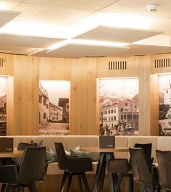 Ein heller Restaurantbereich mit Holzwänden, gepolsterten Sitzbänken und dunklen Stühlen.
