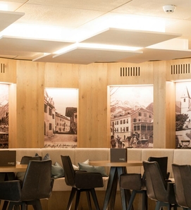 Ein heller Restaurantbereich mit Holzwänden, gepolsterten Sitzbänken und dunklen Stühlen.